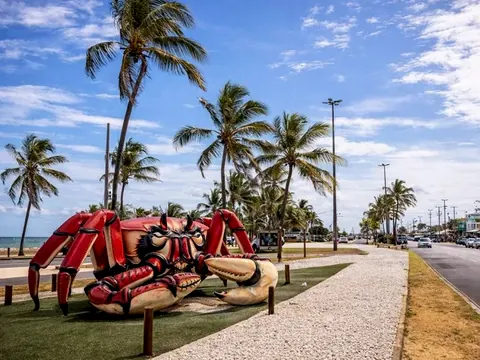 Escultura de caranguejo gigante na orla de Aracaju, com coqueiros e prédios ao fundo