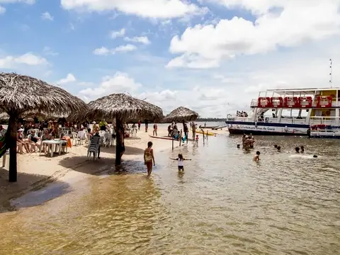 Banco de areia da Croa do Goré com guarda-sóis de palha, pessoas na água rasa e um barco ao fundo